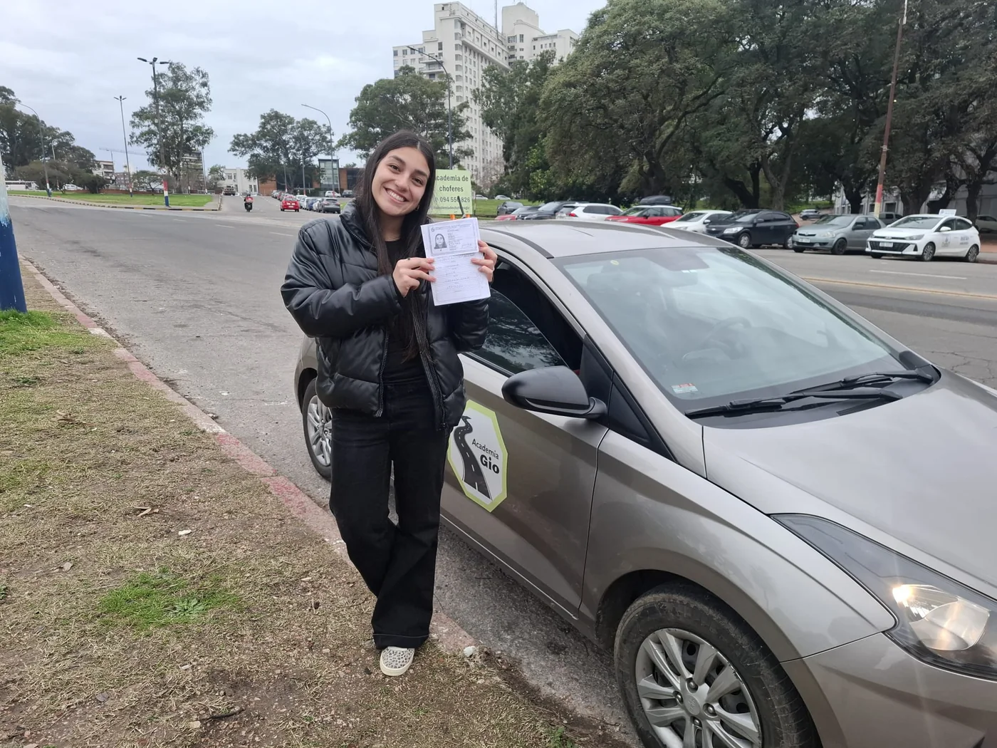 Alumna mostrando su libreta junto al coche escuela