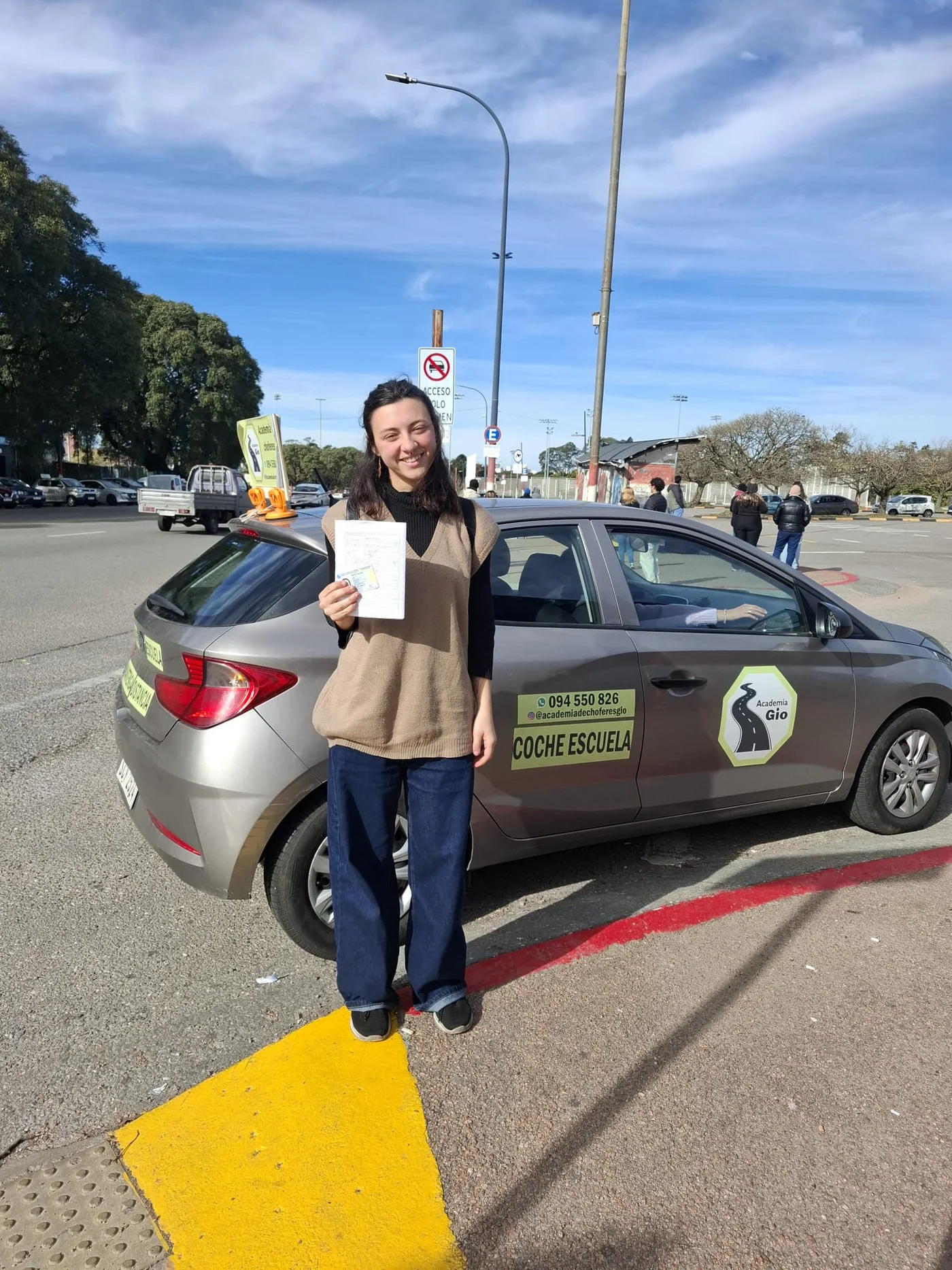 Alumna de Academia Gio junto al coche escuela mostrando su libreta