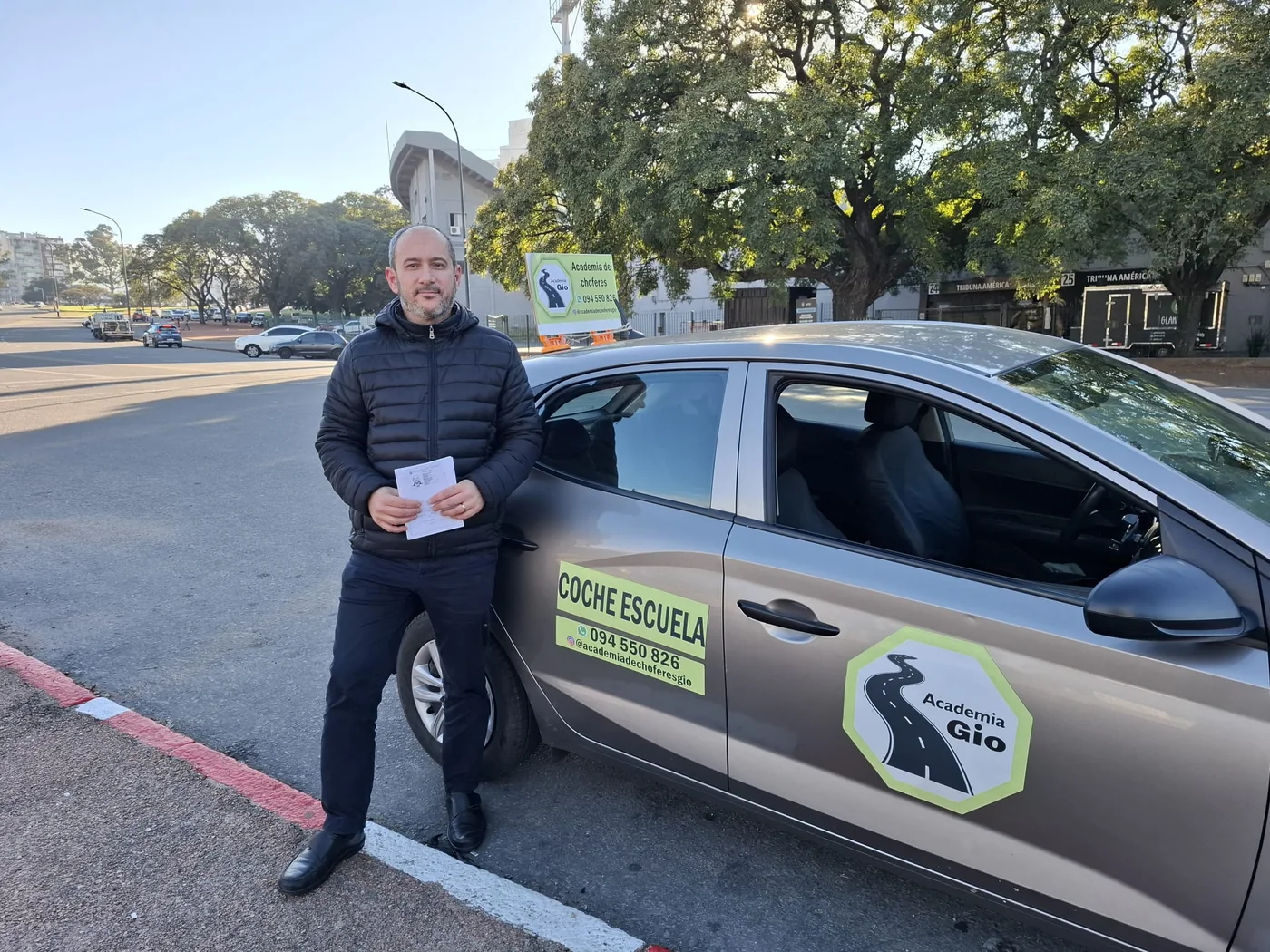 Alumno mostrando su documentación frente al coche escuela